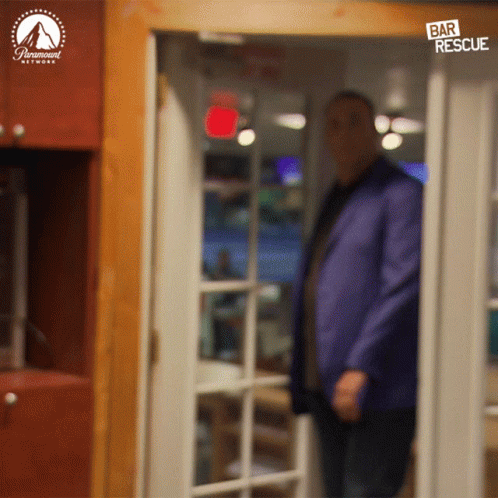 a man in a blue suit is standing in front of a door that says " bar rescue " on it