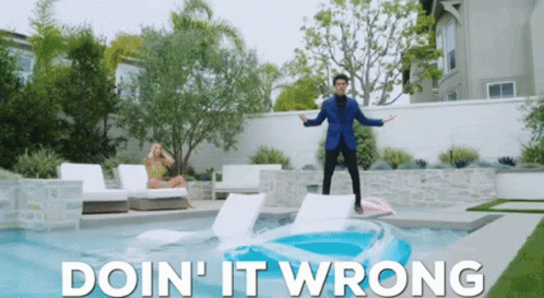 A Man In A Blue Suit Stands On A Raft In A Pool With The Words Doin ' It Wrong Below Him GIF