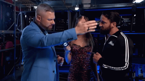 A Man In A Blue Suit Talks To A Woman And Another Man In A Black Jacket With The Word Mele On The Front GIF