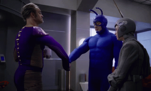 A Man In A Blue Superhero Costume Is Shaking Hands With Two Other Men GIF