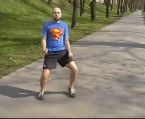 A Man In A Blue Superman Shirt Is Dancing On A Sidewalk . GIF