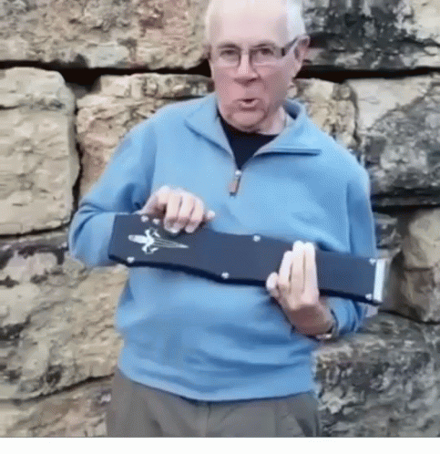 a man in a blue sweater and glasses is holding a black object in his hands