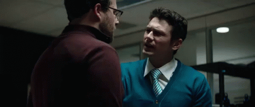A Man In A Blue Sweater And Tie Is Talking To Another Man With The Word Haters Behind Him GIF