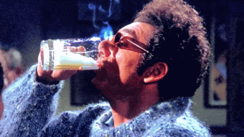 A Man In A Blue Sweater Drinks From A Glass GIF