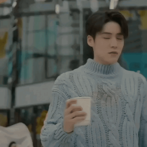 A Man In A Blue Sweater Is Holding A Cup Of Coffee In A Restaurant . GIF