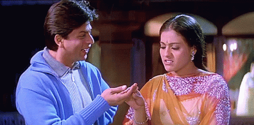 A Man In A Blue Sweater Is Holding A Woman 'S Hand In Front Of Her Face GIF