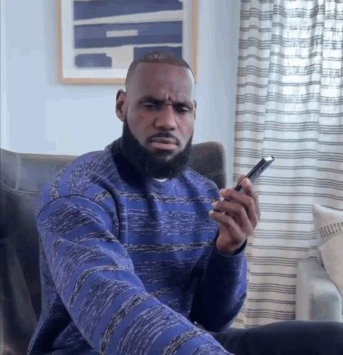 A Man In A Blue Sweater Is Looking At His Phone GIF