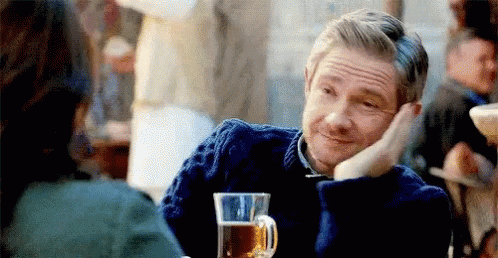 A Man In A Blue Sweater Is Sitting At A Table With A Glass Of Beer In Front Of Him . GIF