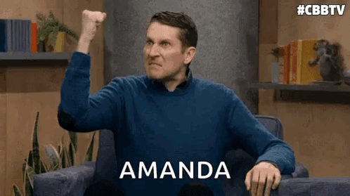 A Man In A Blue Sweater Is Sitting In A Chair With His Fist In The Air And The Word Amanda Behind Him . GIF