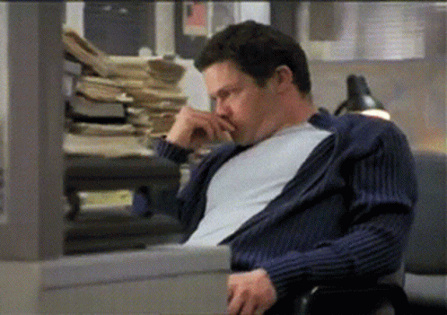 A Man In A Blue Sweater Is Sitting In Front Of A Pile Of Papers GIF
