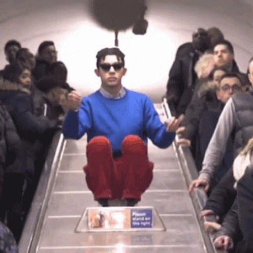 A Man In A Blue Sweater Is Sitting On An Escalator GIF