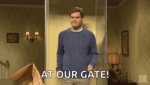 A Man In A Blue Sweater Is Standing In A Doorway With The Words `` At Our Gate '' Written On It . GIF