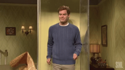 A Man In A Blue Sweater Is Standing In A Room With The Letters Snl On The Wall GIF