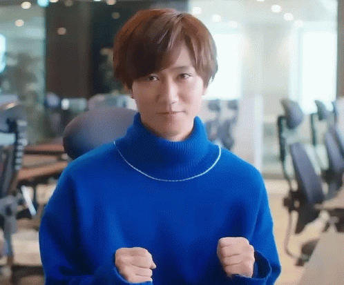 A Man In A Blue Sweater Is Standing In An Office With His Fists Up . GIF