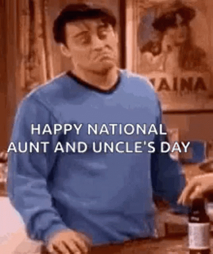 A Man In A Blue Sweater Is Standing In Front Of A Counter And A Bottle Of Wine . GIF