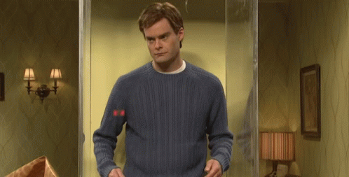 A Man In A Blue Sweater Is Standing In Front Of A Glass Door In A Room . GIF