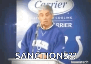 A Man In A Blue Sweater Is Standing In Front Of A Podium With The Words Sanctions On It . GIF