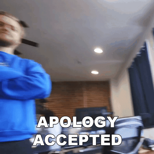 Man In Blue Sweater Standing In Front Of Apology Sign GIF