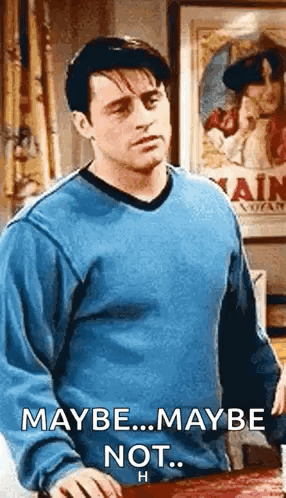 A Man In A Blue Sweater Is Standing In Front Of A Table And A Poster . GIF