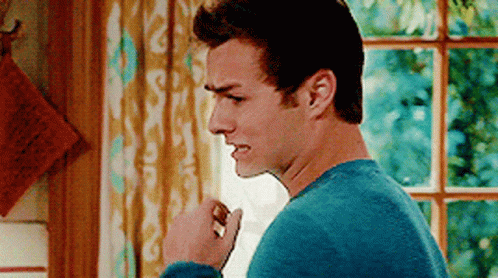 A Man In A Blue Sweater Is Standing In Front Of A Window With His Fist In The Air . GIF