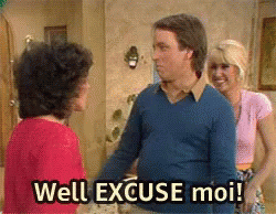 A Man In A Blue Sweater Says " Well Excuse Moi " In Front Of Two Women GIF