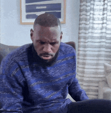 A Man In A Blue Sweater Sits In Front Of A Laptop Computer GIF