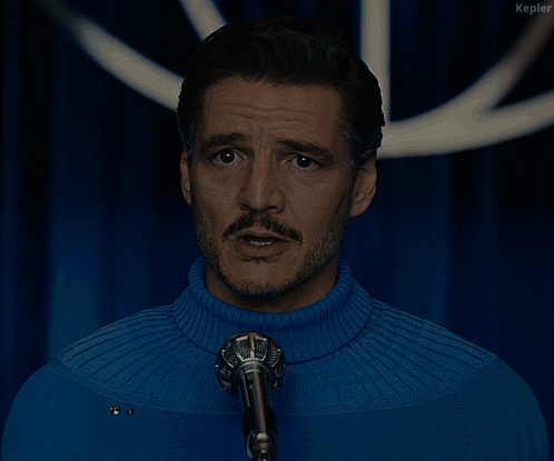 A Man In A Blue Sweater Stands In Front Of A Microphone With The Words We Will Protect You Below Him GIF