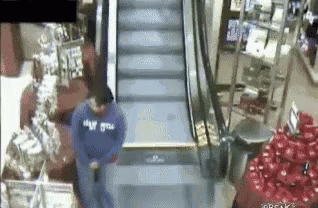 A Man In A Blue Sweatshirt Is Standing On An Escalator . GIF
