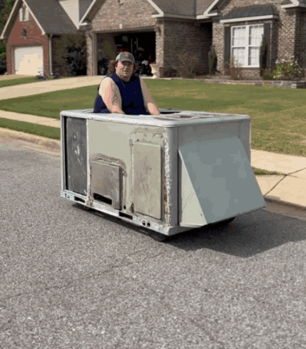 A Man In A Blue Tank Top Is Driving A Small Vehicle On The Street GIF
