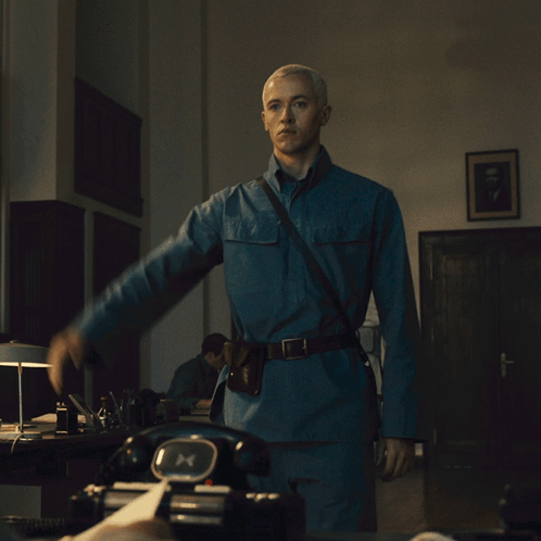 A Man In A Blue Uniform Is Standing In Front Of A Black Telephone GIF