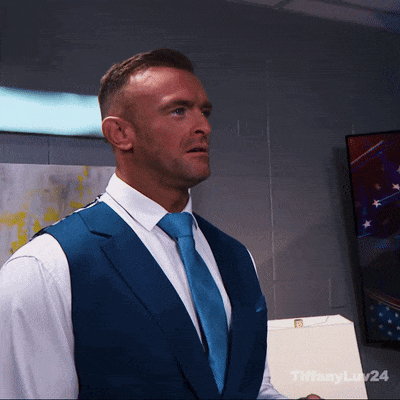 A Man In A Blue Vest And Tie Is Standing In Front Of A Wall With Tiffanylaw24 Written On It GIF