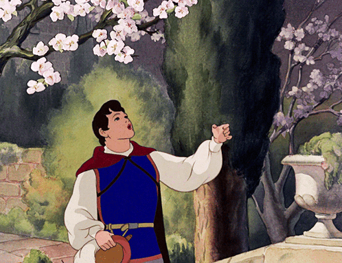 A Man In A Blue Vest Is Looking Up At A Tree GIF