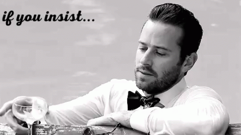 A Man In A Bow Tie Is Sitting At A Table With A Glass Of Wine In His Hand . GIF