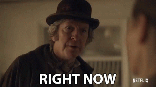 A Man In A Bowler Hat Is Talking To Another Man And Says Right Now . GIF