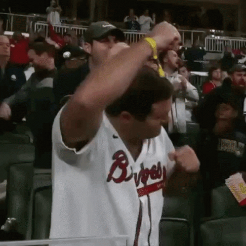 A Man In A Braves Jersey Is Standing In The Stands With His Arms In The Air . GIF