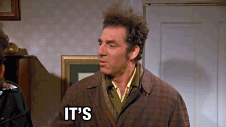 A Man In A Brown Coat Is Standing In Front Of A Door With The Words `` It 'S '' Written On It . GIF