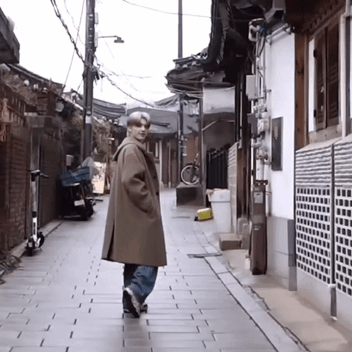 A Man In A Brown Coat Is Walking Down A Narrow Alleyway GIF