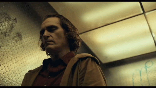 A Man In A Brown Coat Stands In A Dark Room GIF
