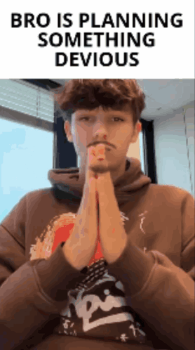 a man in a brown hoodie is praying with the words bro is planning something devious behind him