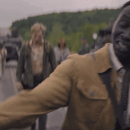 A Man In A Brown Jacket And Tie Is Standing In Front Of A Crowd . GIF