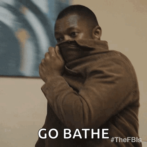 A Man In A Brown Jacket Is Covering His Face With His Jacket And Says Go Bathe GIF