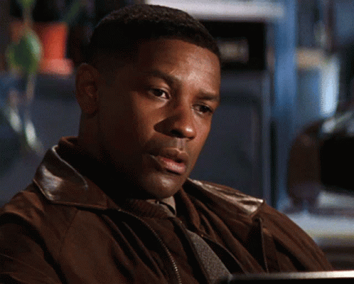 A Man In A Brown Jacket Is Sitting At A Desk GIF