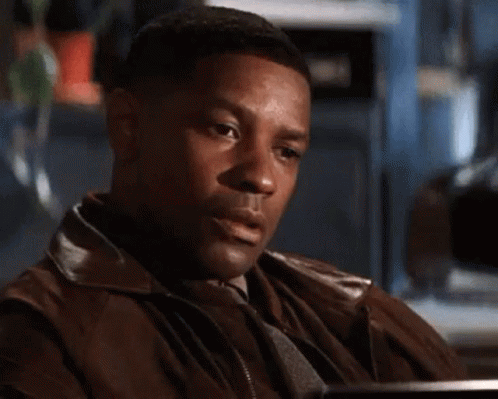 A Man In A Brown Jacket Is Sitting At A Table With His Hands On His Chest . GIF