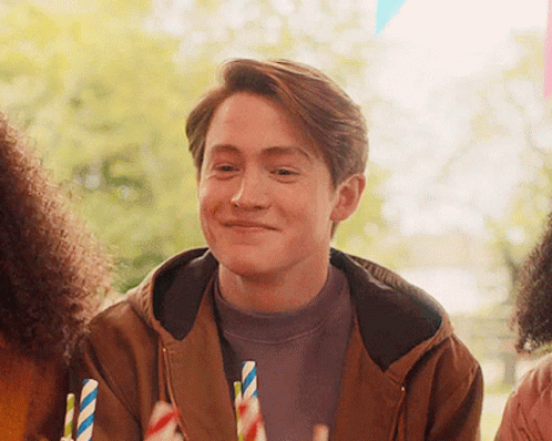 A Man In A Brown Jacket Is Smiling While Holding A Straw GIF