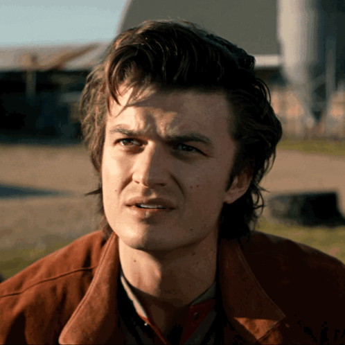 A Man In A Brown Jacket Looks At The Camera GIF