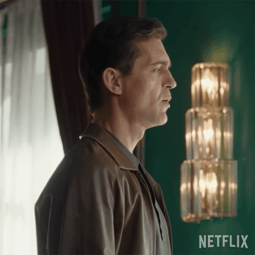 A Man In A Brown Jacket Stands In Front Of A Netflix Sign GIF