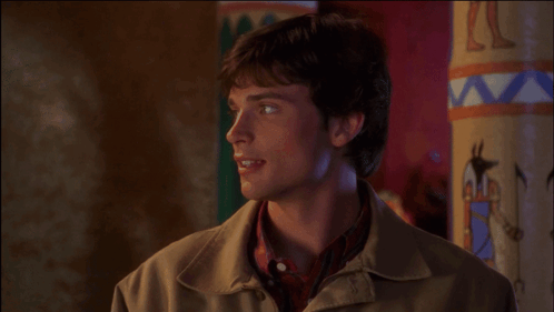 A Man In A Brown Jacket Stands In Front Of A Wall With A Painting Of A Pyramid On It GIF