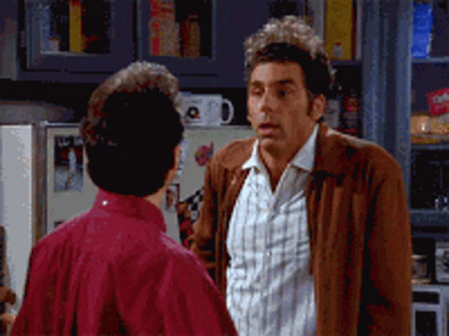 A Man In A Brown Jacket Talks To Another Man In A Kitchen GIF