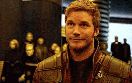A Man In A Brown Leather Jacket Is Smiling In Front Of A Group Of Statues . GIF