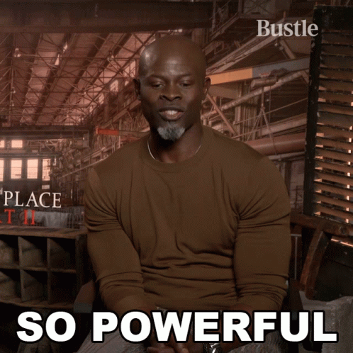 A Man In A Brown Shirt Is Sitting In Front Of A Poster That Says " So Powerful " GIF